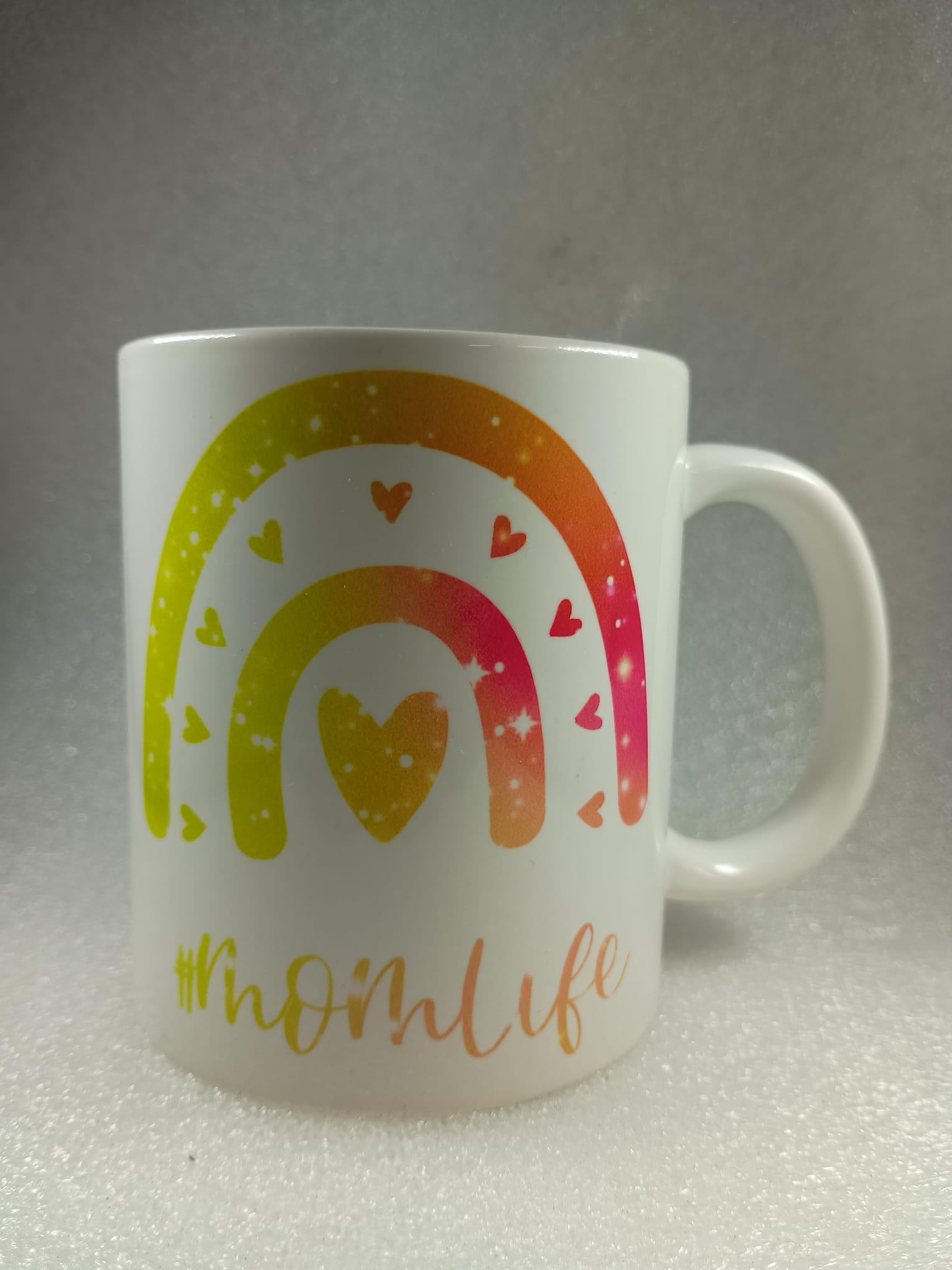 White mug with a colorful rainbow and heart design, featuring the text 'mom life'.